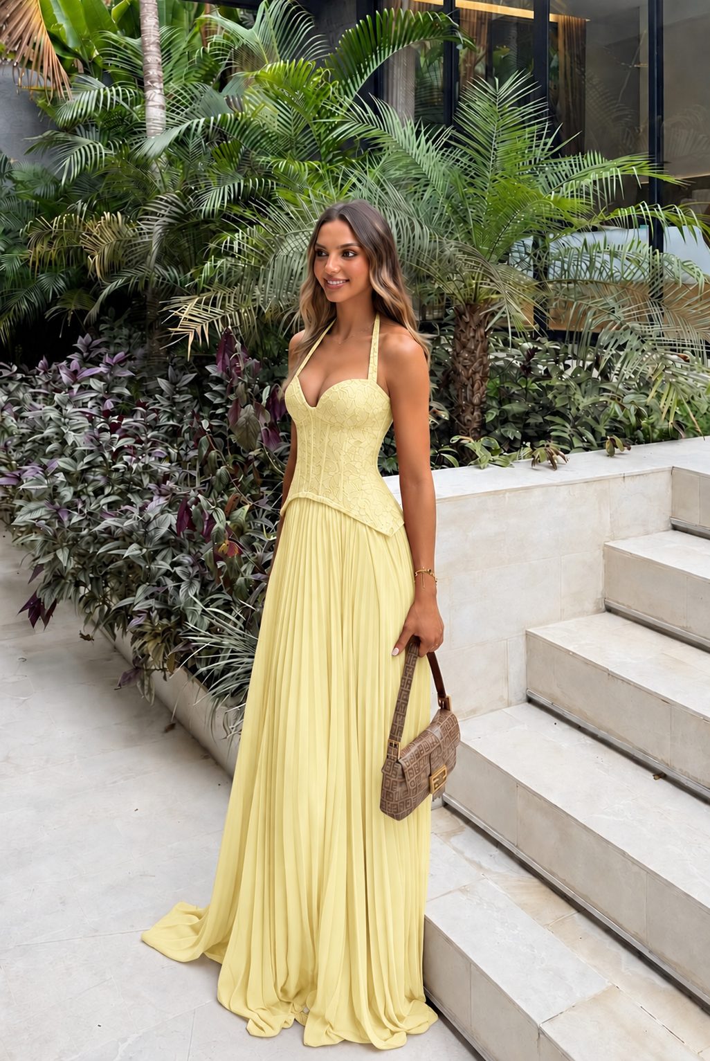 Enid Pleated Corset Maxi Dress – Yellow worn beside tropical greenery and pale stone steps